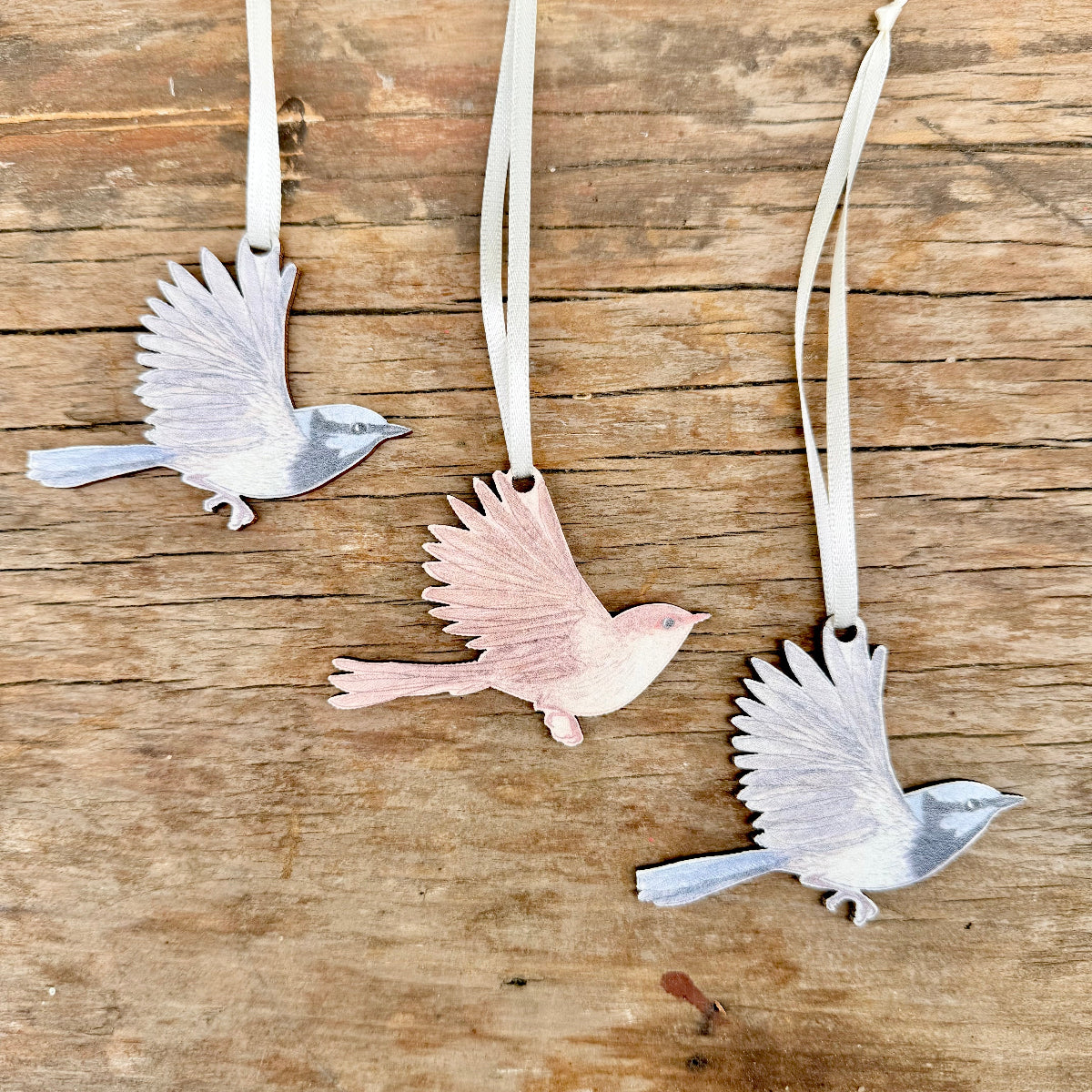 Three superb fairywren  ornaments displayed on a rustic wooden surface, each attached to a cream ribbon.
