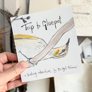 Book titled 'Trip to Gluepot' held by a hand with a bird illustration on the cover.