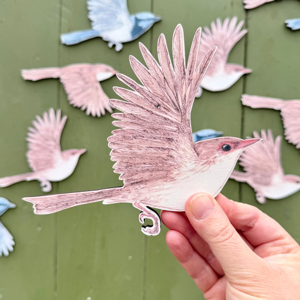 a hand holds one of the wooden wall decorations featuring a brown superb fairywren